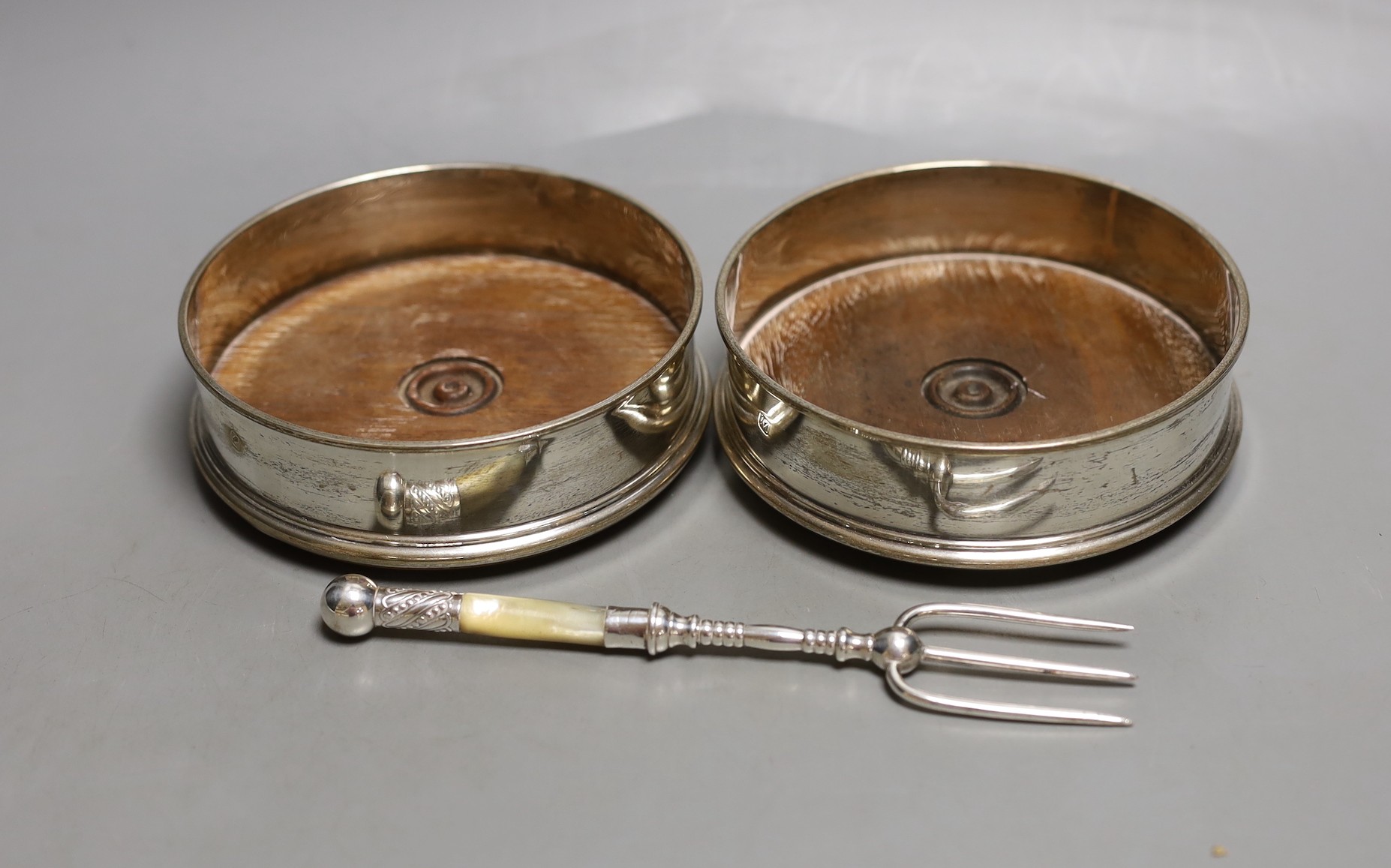 A modern pair of silver mounted wine coasters, London, 1985/6, diameter 12.5cm and a white metal and mother of pearl toasting fork.